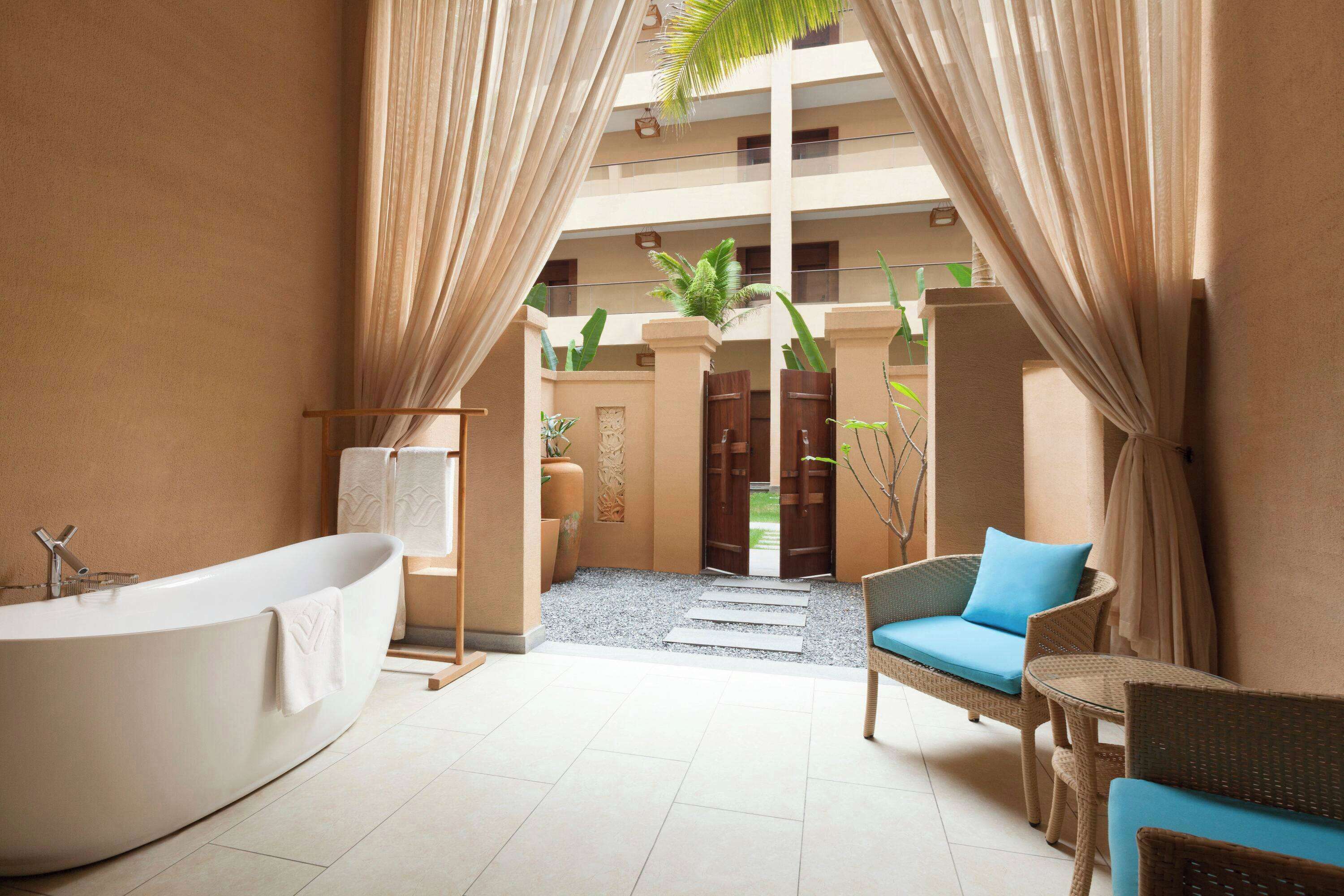 Een badkamer in spa-stijl met een vrijstaand bad, een rieten stoel met kussen en een klein tafeltje.