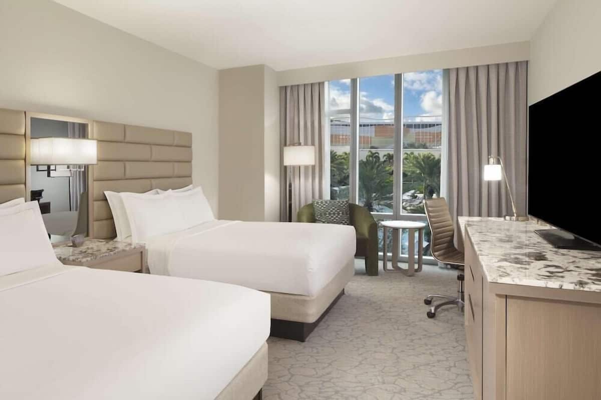 A hotel room with two beds, a desk, a chair, and a TV.