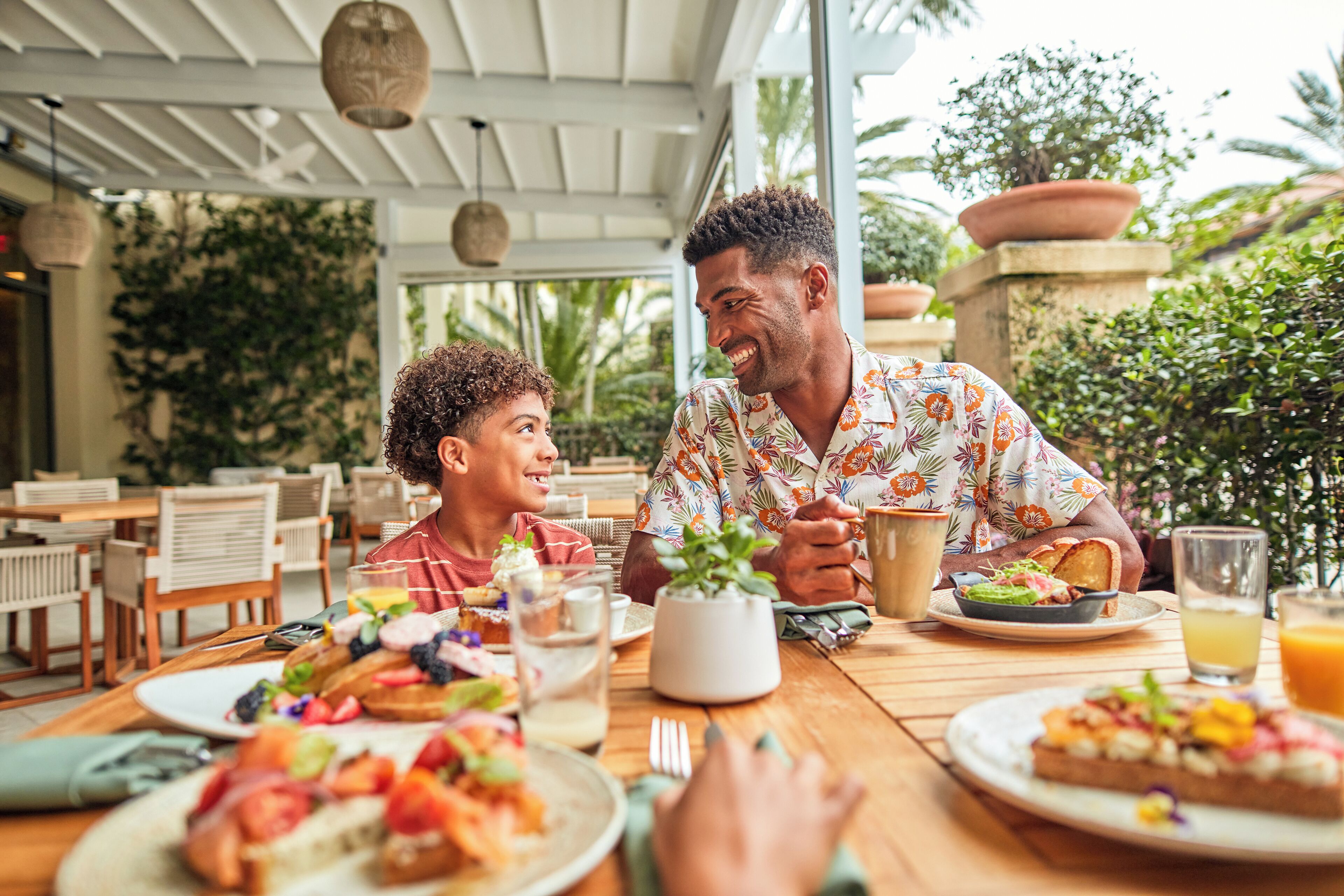 Comedor con mesas de madera, plantas en macetas y ambiente tropical.