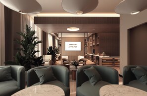A modern hotel lounge with green sofas, a marble coffee table, and a large screen displaying 'THE CLUB AT HILTON'.