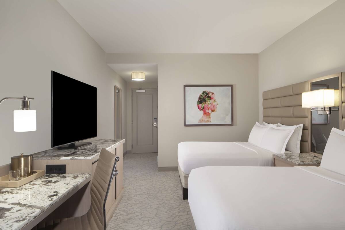 Habitación de hotel con dos camas, televisión, escritorio con encimera de mármol, baño y un cuadro en la pared.