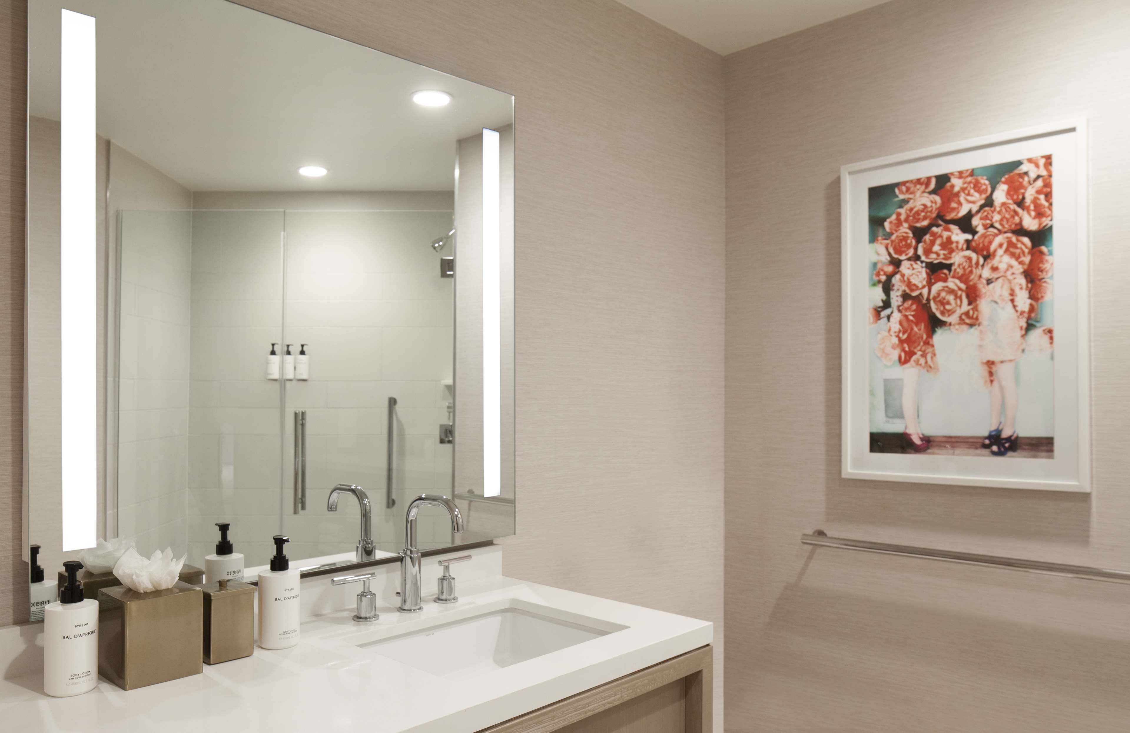 A modern bathroom with a large mirror, a sink, and a framed floral artwork on the wall.