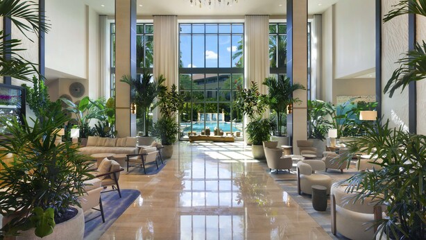 Un amplio lobby con una zona de estar central, ventanas grandes y vista a la piscina.