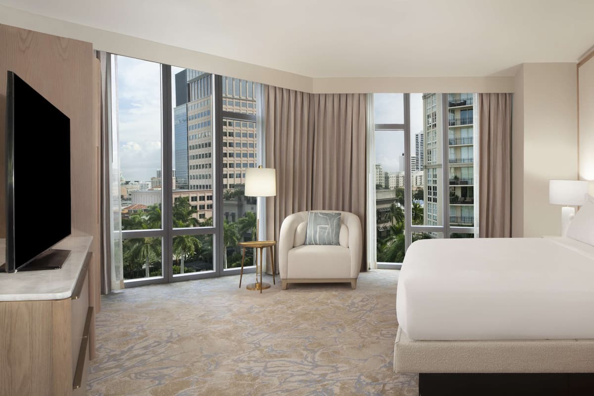 Una habitación de hotel con una cama grande, una silla, un televisor y vistas a edificios altos.