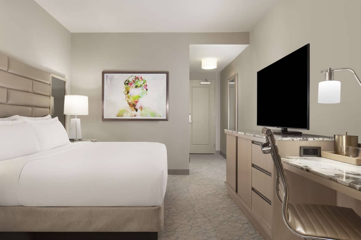 Habitación de hotel con cama, televisor, baño con espejo y un cuadro en la pared.
