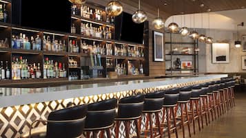 A bar area with multiple stools, shelves stocked with bottles, and hanging spherical light fixtures.