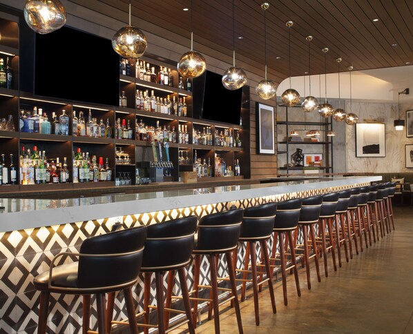 A bar area with multiple stools, shelves stocked with bottles, and hanging spherical light fixtures.