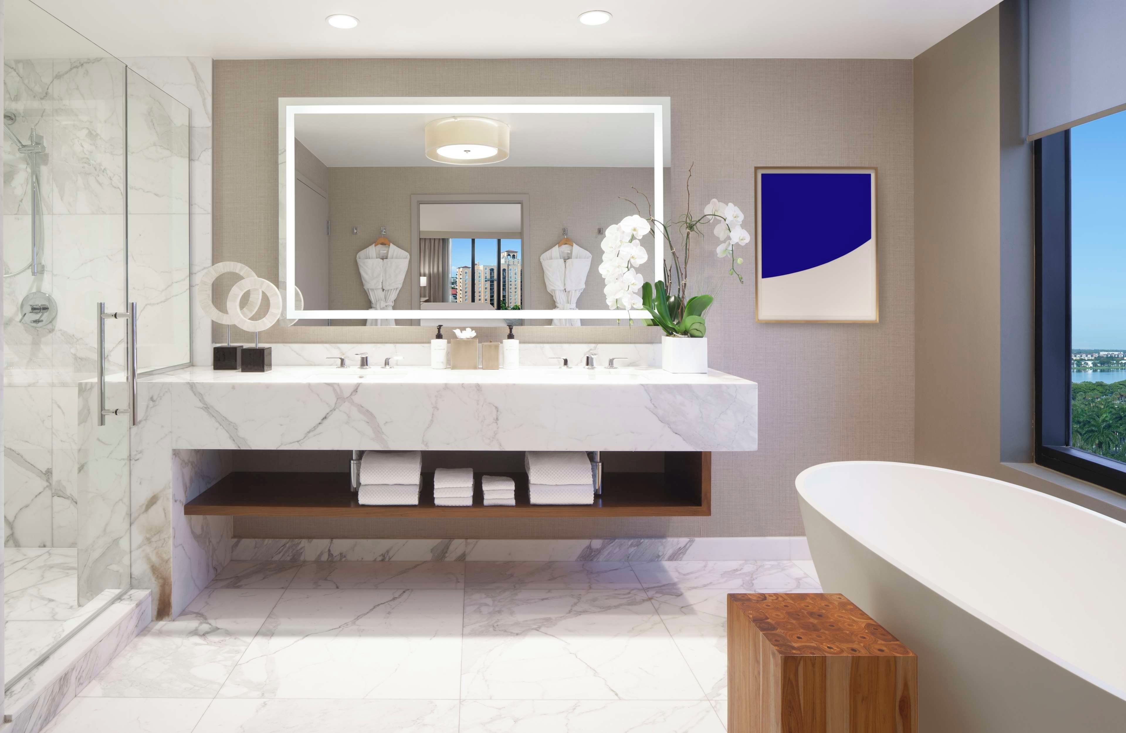 A modern bathroom with a large mirror, two sinks, a bathtub, and a shower.