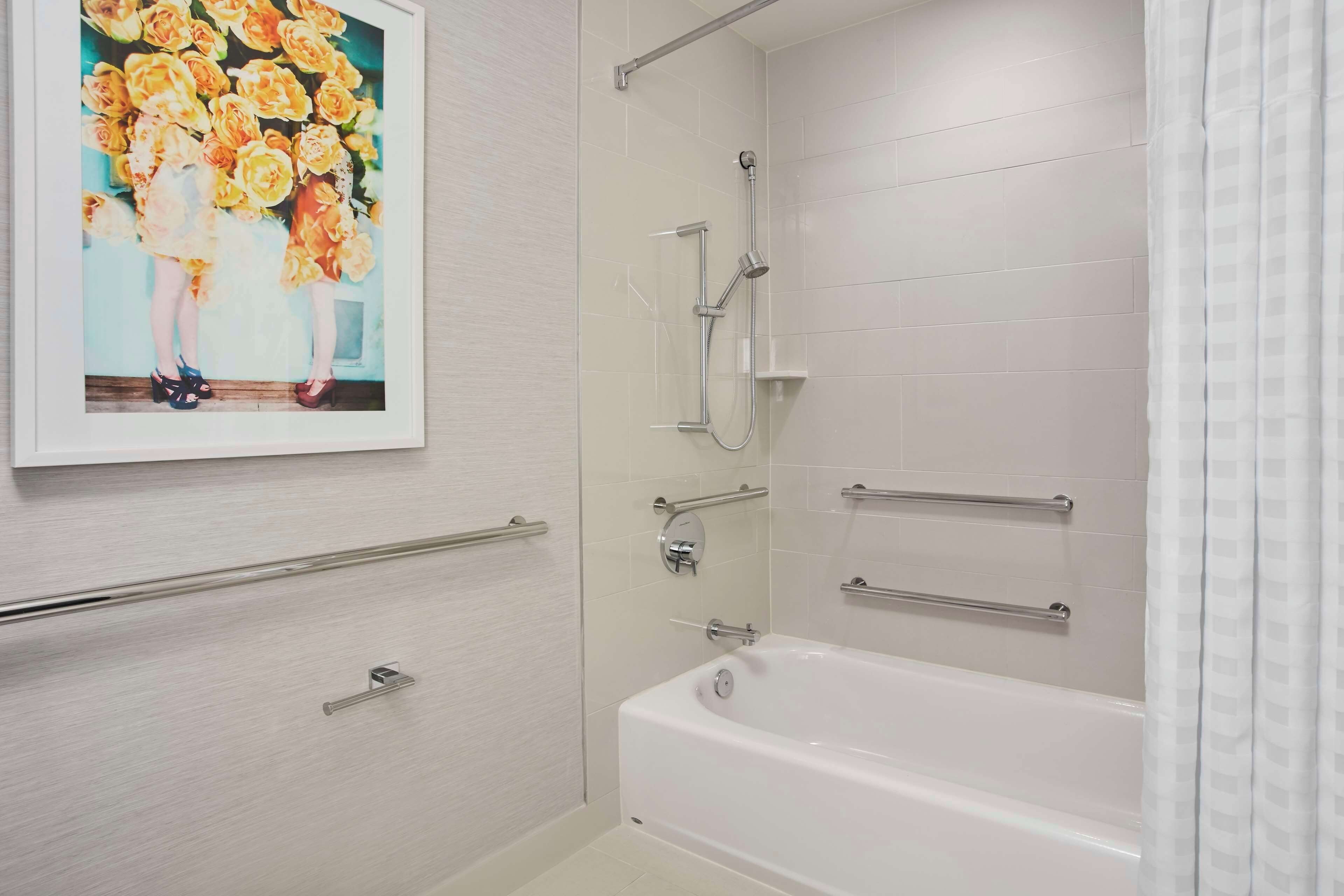 A bathroom with a white bathtub, a shower with a handheld showerhead, and a wall-mounted towel rack.