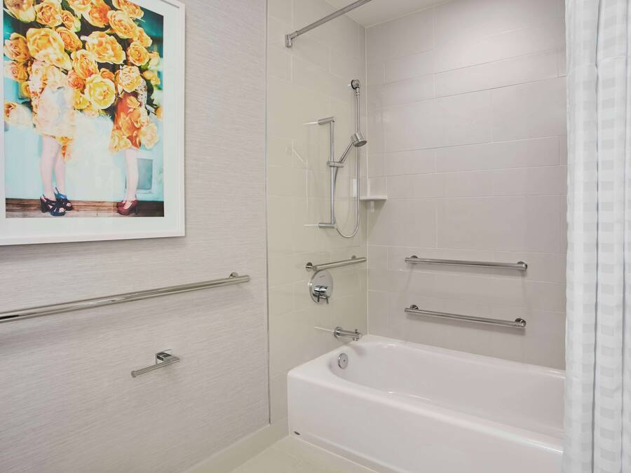 A bathroom with a white bathtub, a shower with a handheld showerhead, and a wall-mounted towel rack.