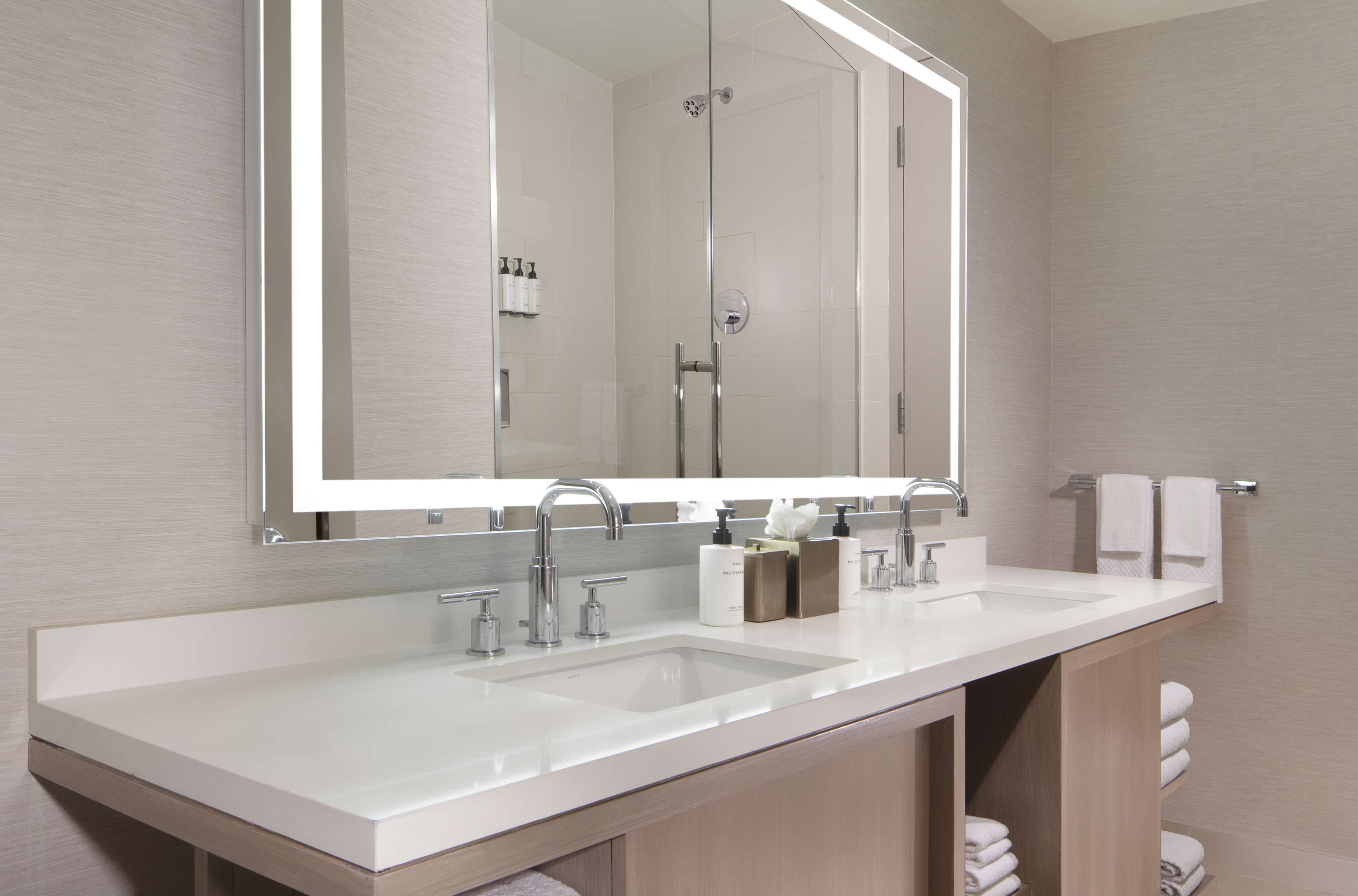 A modern bathroom with a large mirror, two sinks, and a shower.