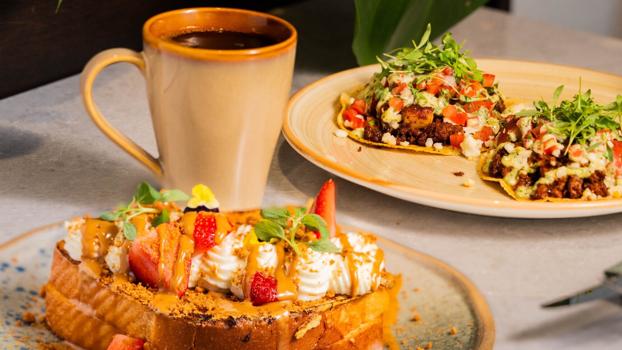 A dessert with strawberries and caramel, a mug of coffee, and a plate with a dish topped with greens and diced tomatoes.