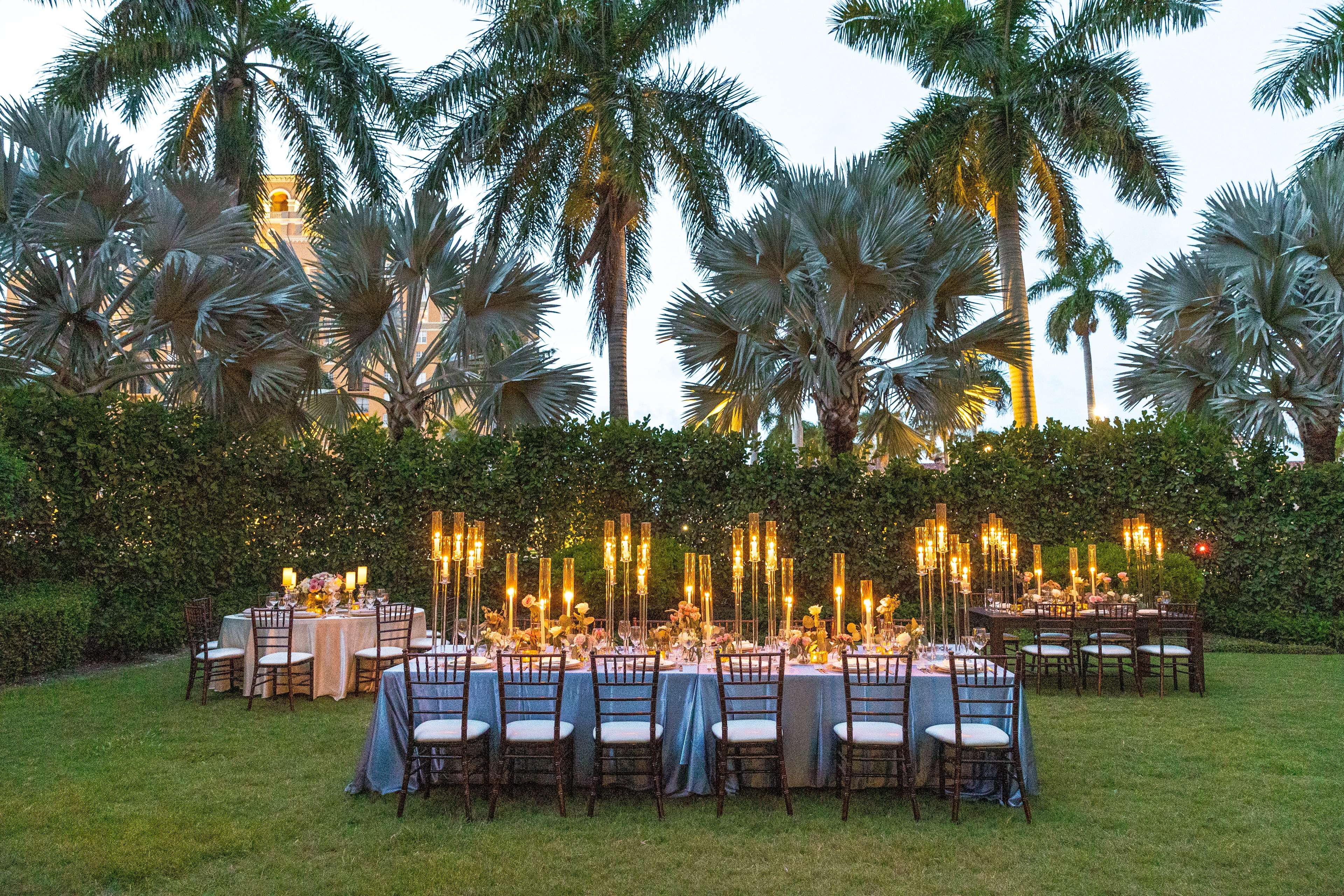 An outdoor dining area with tables set for guests, surrounded by lush greenery and palm trees.