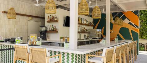 Un espace bar extérieur doté d’un long comptoir, de chaises en osier et de lampes suspendues en osier.