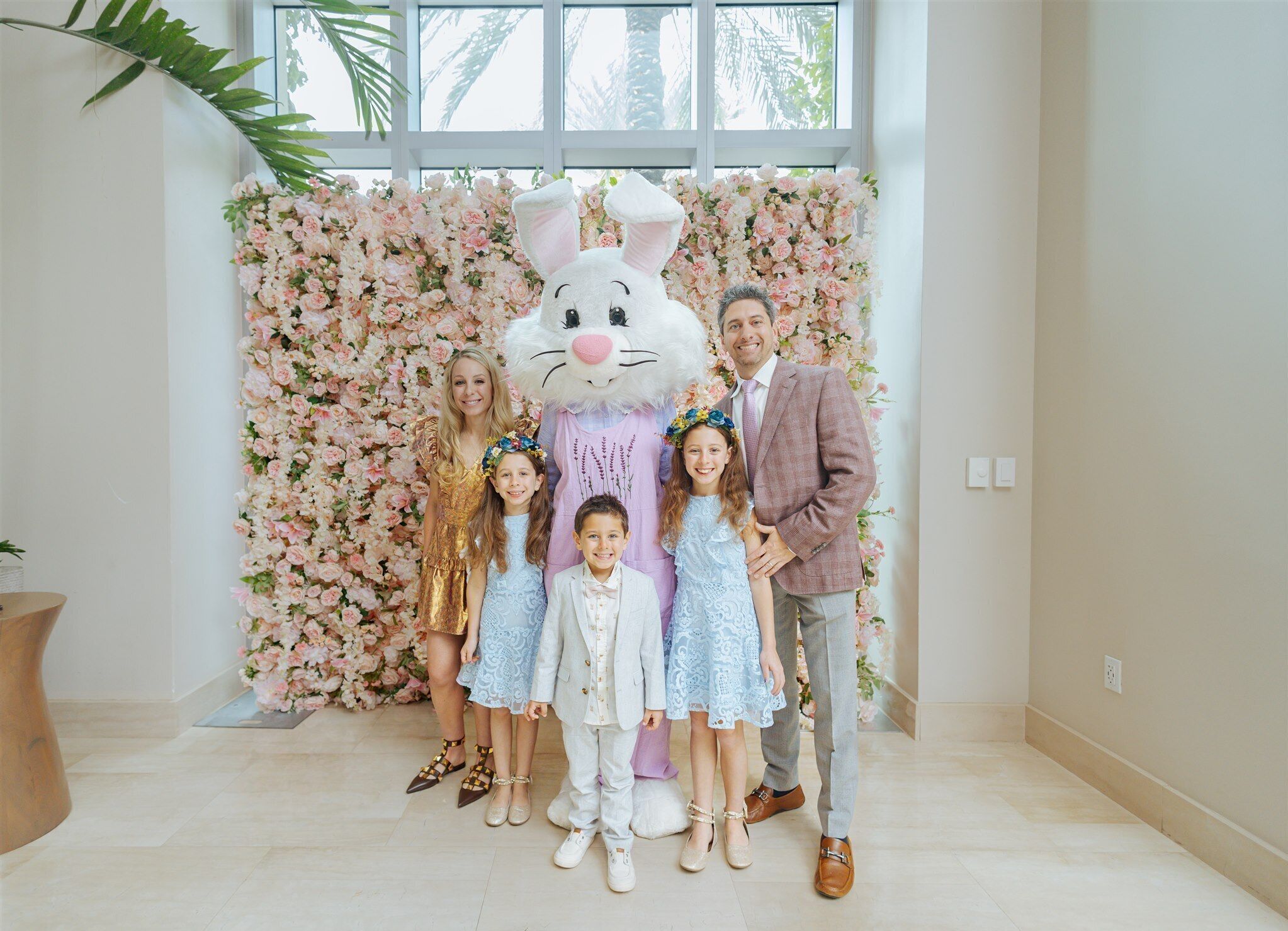 A group of people standing in front of a floral backdrop with a large white rabbit mascot.