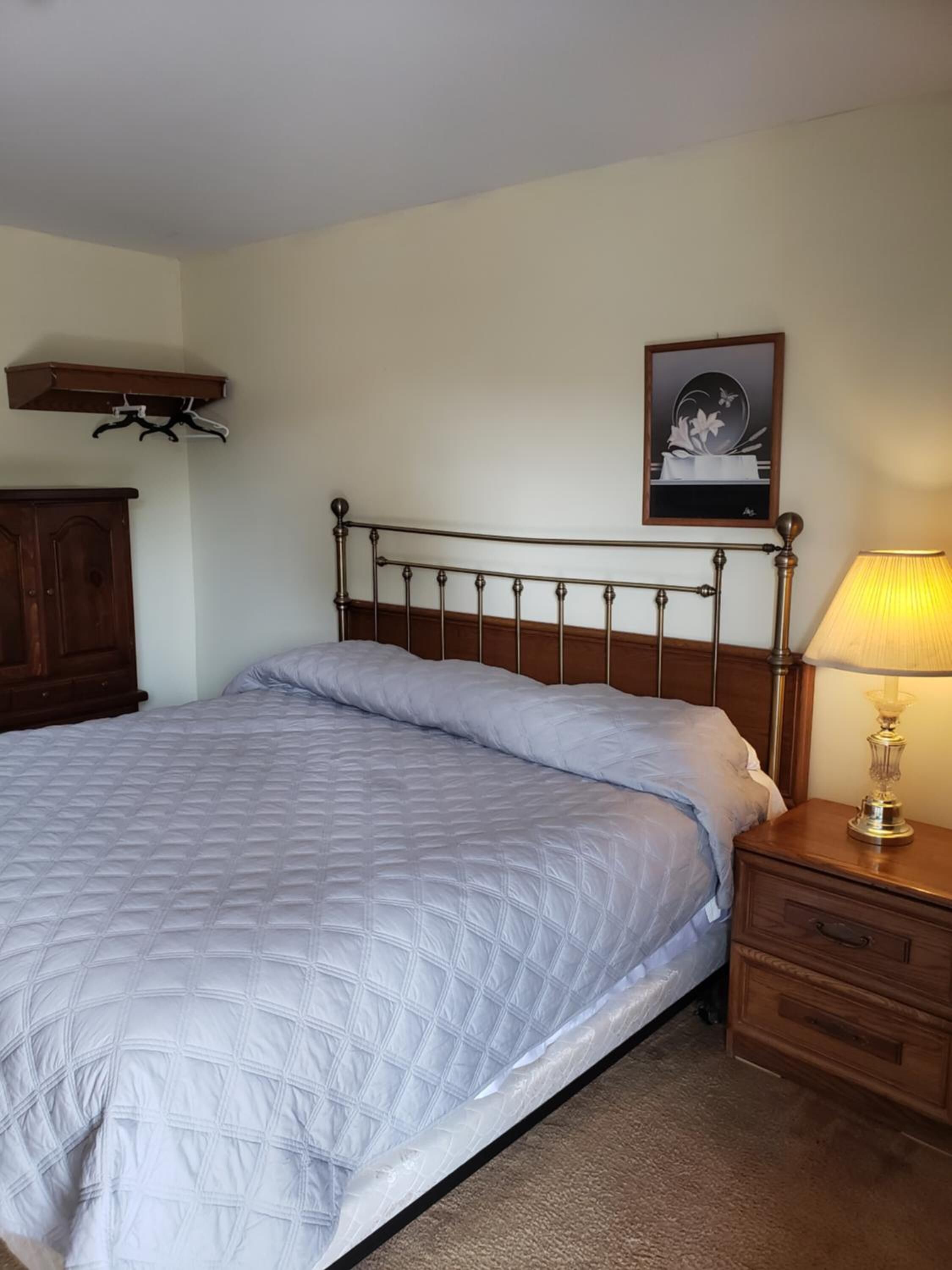 A neatly made bed with a quilted cover, a wooden headboard, a bedside lamp, and a wooden nightstand with drawers.
