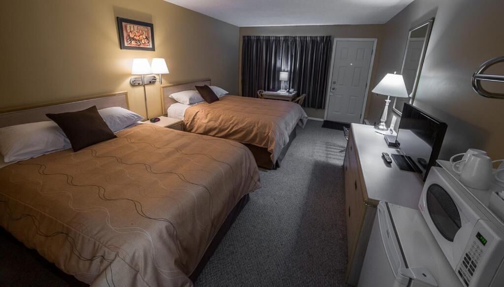 A hotel room with two beds, a desk with a computer and a microwave, and a door with curtains.