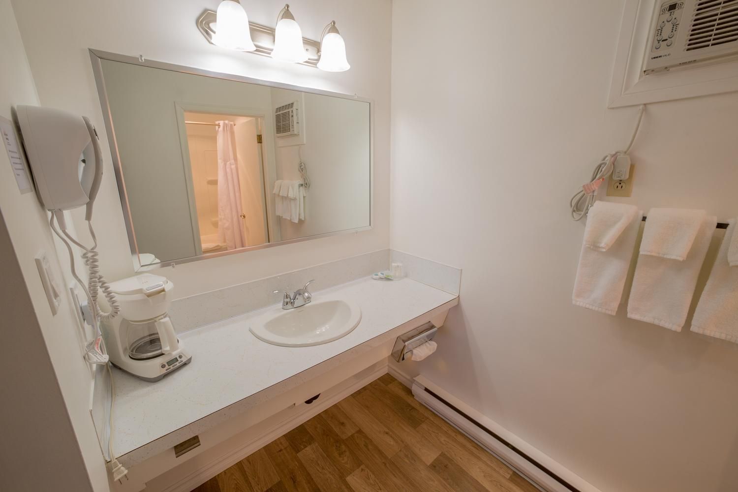 Une salle de bain avec un lavabo blanc, un miroir, un sèche-cheveux et un porte-serviettes.