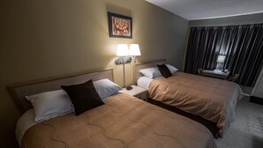 Una habitación de hotel con dos camas, una mesita de noche con lámpara, una silla y una ventana con cortinas.