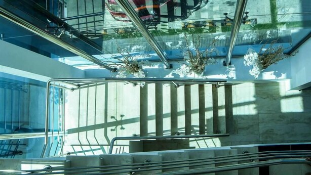 A modern interior with a glass railing, a marble staircase, and a view of the sky and greenery outside. - Dpravia Hotel SRL (Bani)