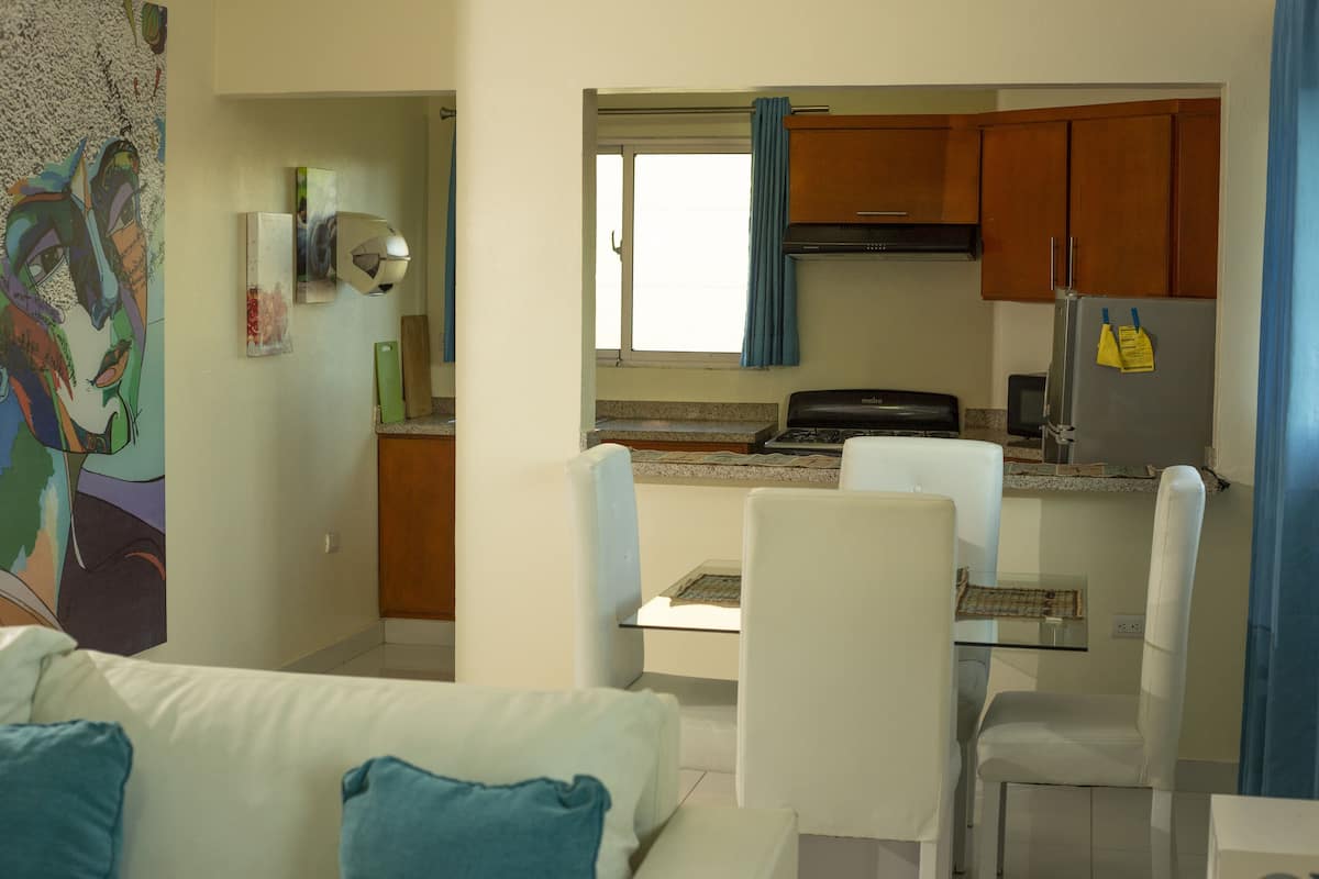 A compact living space with a kitchenette, a dining area with a glass table, and a sofa with blue cushions.