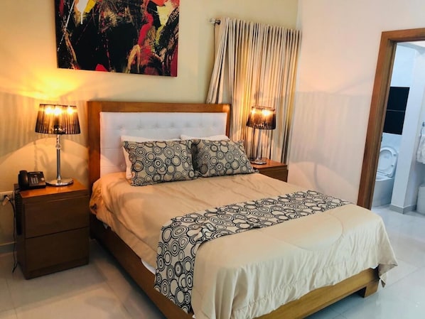 A hotel room with a large bed, two bedside tables, and a painting on the wall.