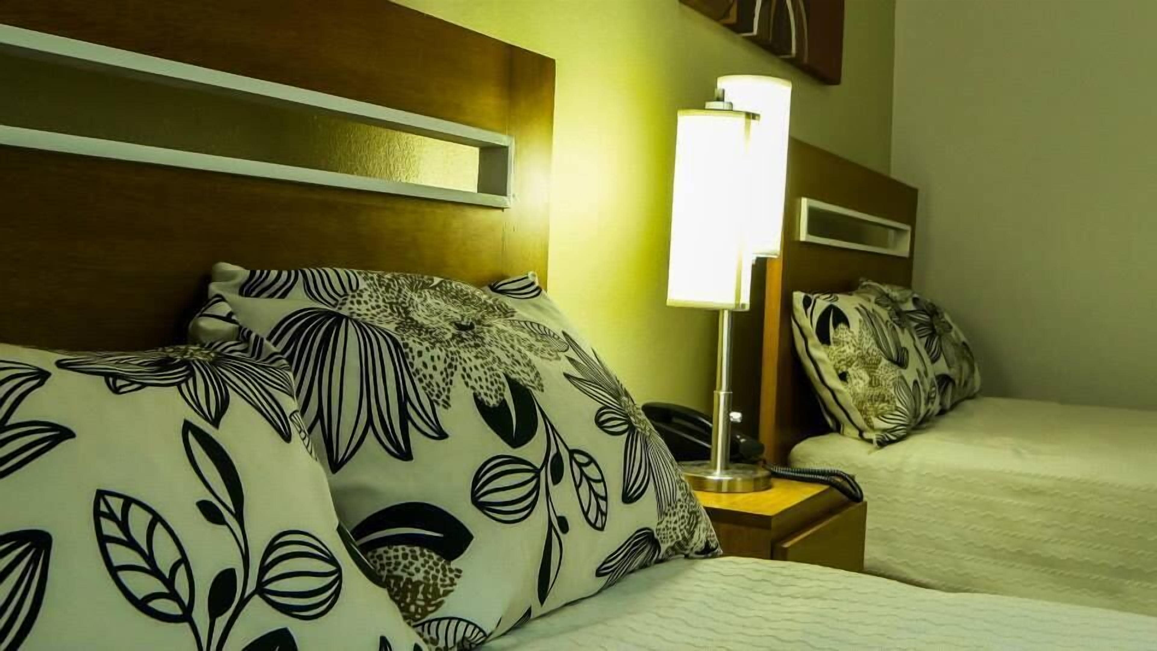 A hotel room with a bed featuring black and white floral patterned bedding, a bedside lamp, and a nightstand with a telephone.