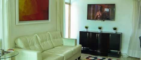 A living room with a white sofa, a black entertainment unit, a TV, and a red abstract painting.