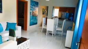 A modern living room with a white sofa, a glass coffee table, and a dining area with white chairs. - Dpravia Hotel SRL (Bani)