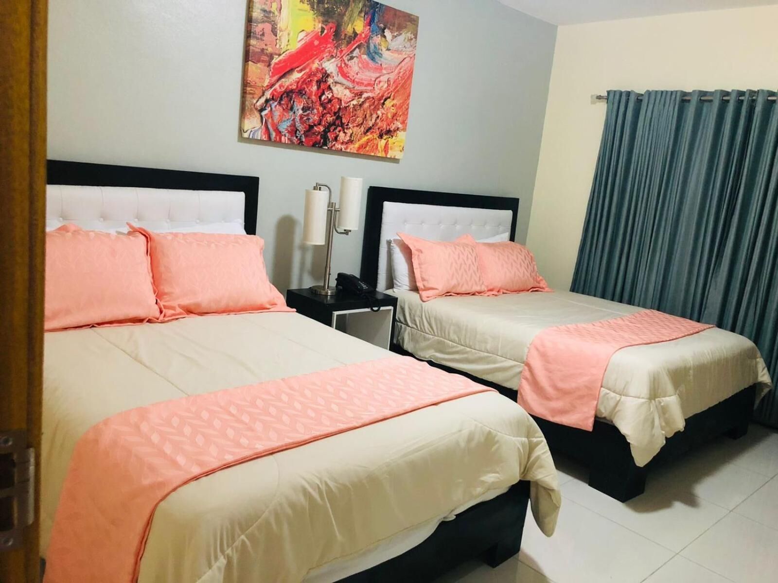 A hotel room with two beds, each with a white headboard, peach bedding, and a painting above the beds.