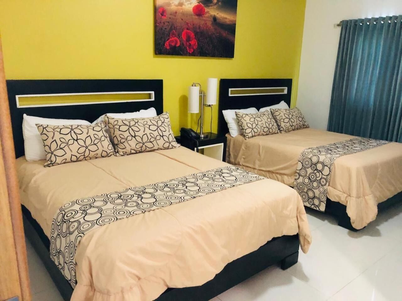 A hotel room with two beds, each with patterned bedding and headboards. There is a painting on the wall above the beds and a nightstand with a lamp between them.