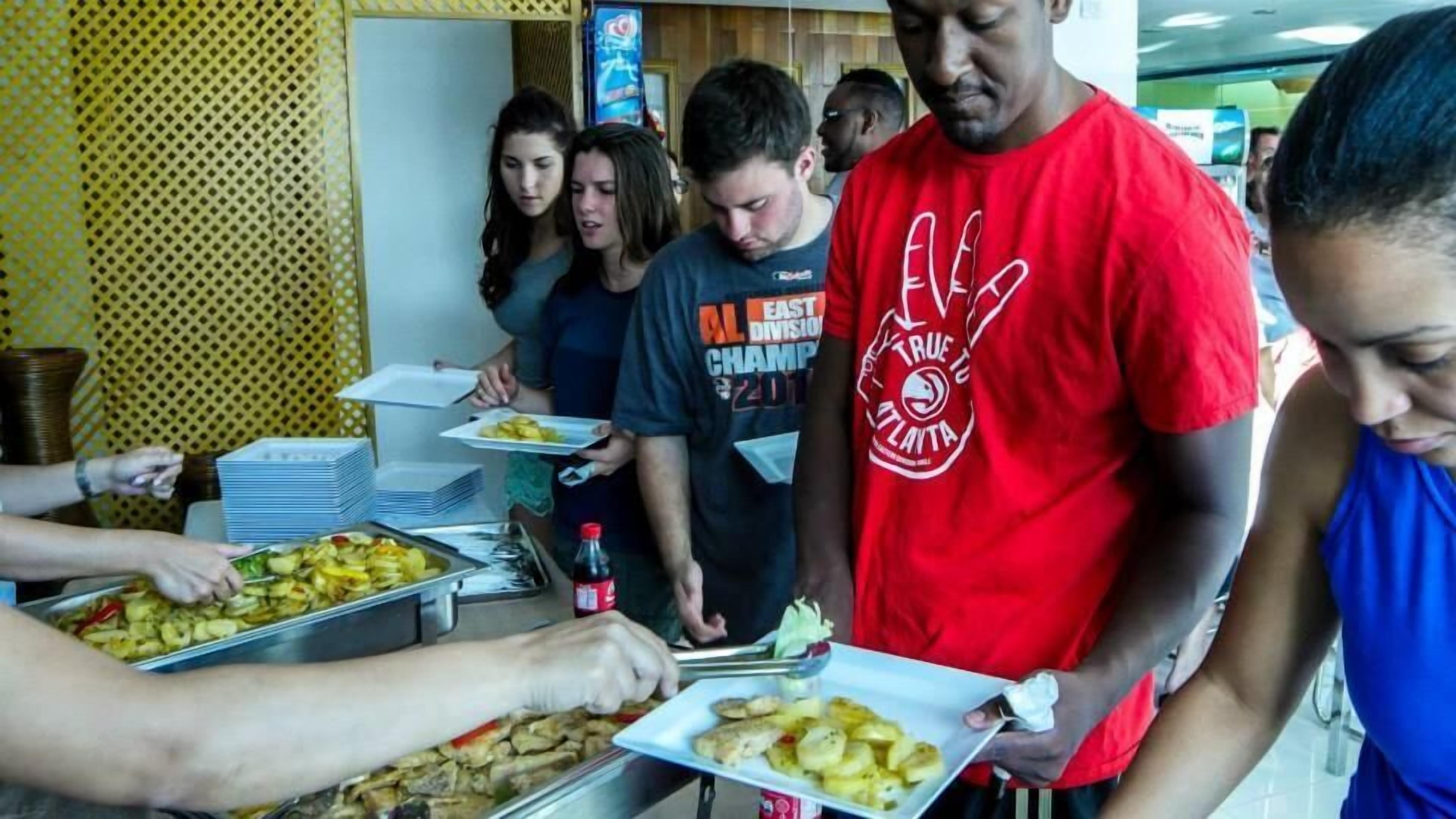 Montaje de bufé con diferentes alimentos y personas servándose.