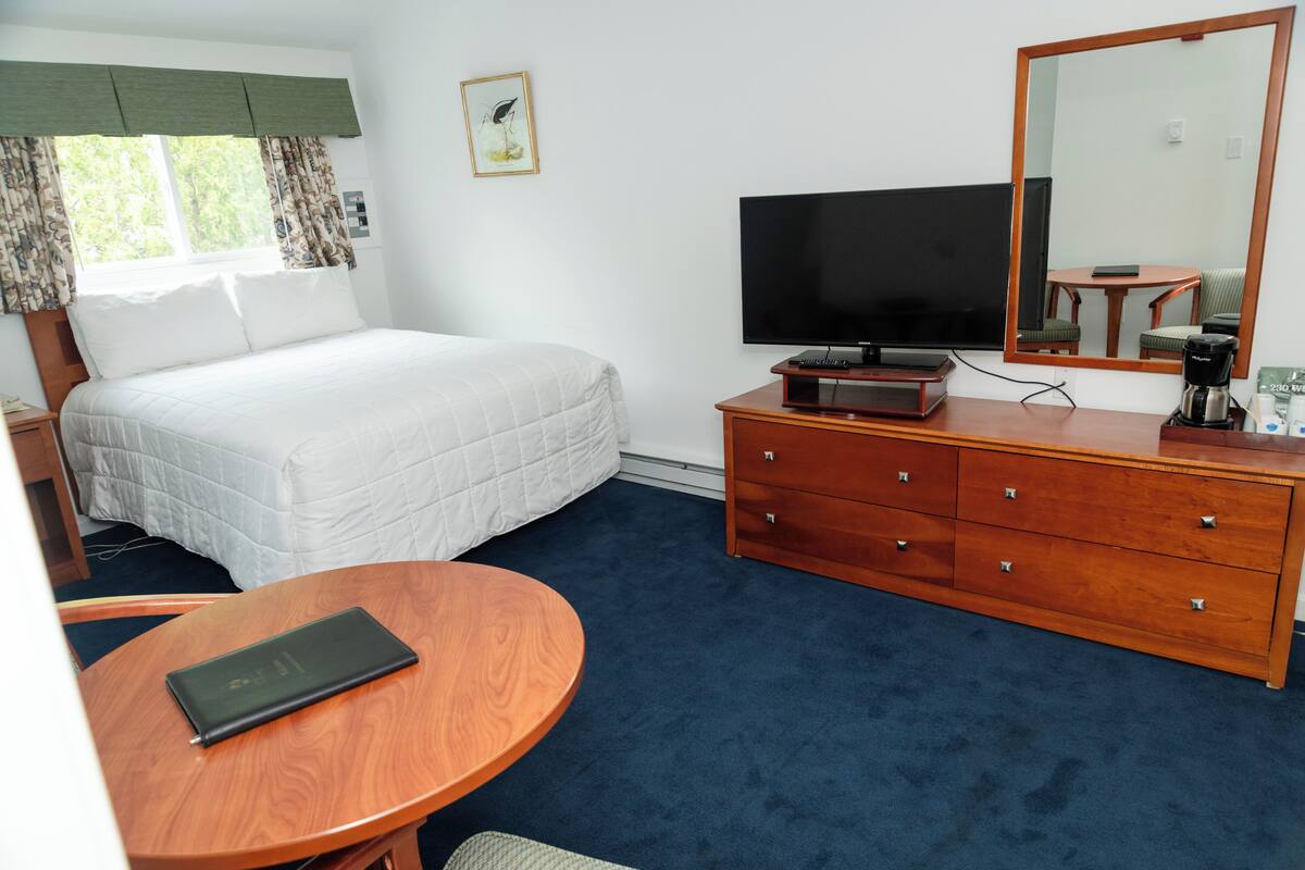 A hotel room with a bed, a television, a dresser, and a round table.