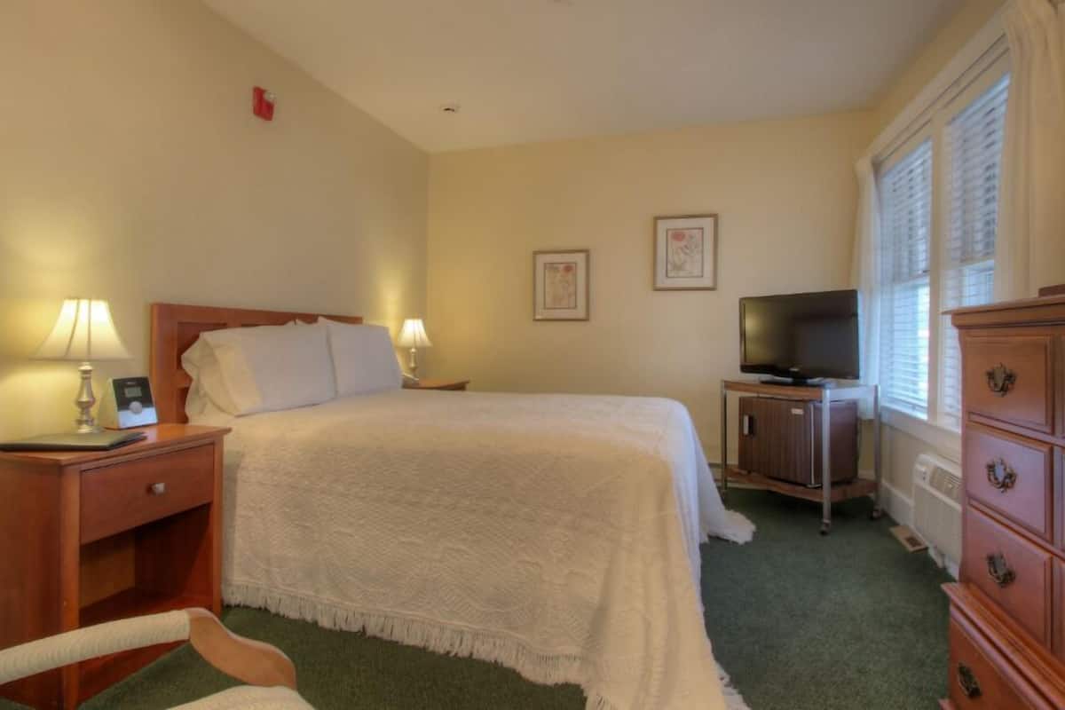 A hotel room with a bed, bedside lamps, a television, a dresser, and a framed picture on the wall.