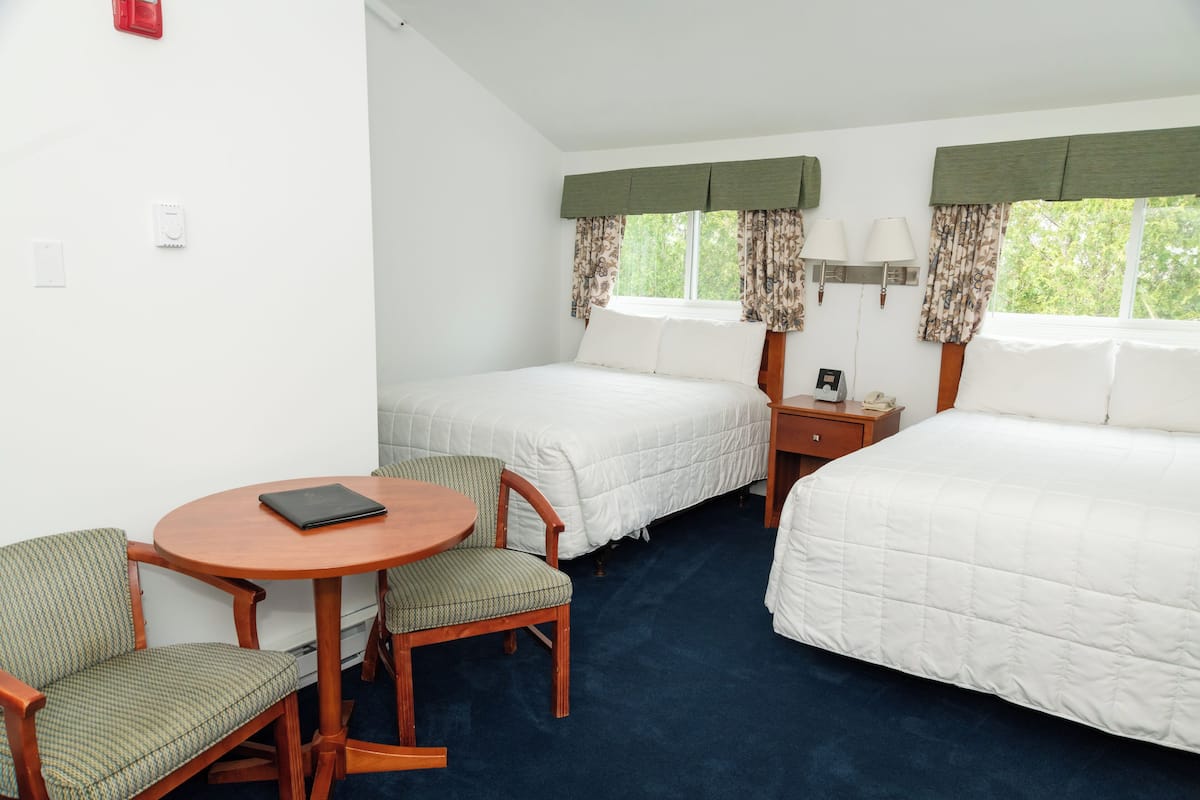 A hotel room with two beds, a small table with chairs, and a nightstand with a lamp.