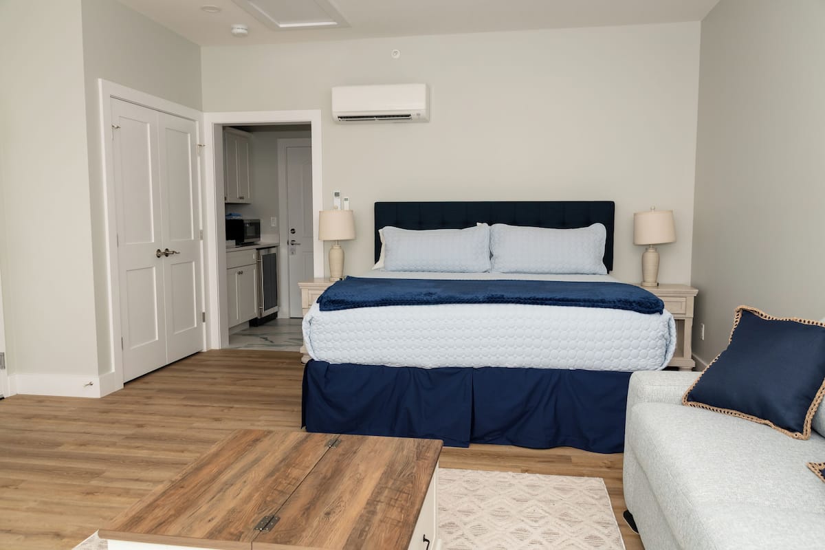 A bedroom with a bed, bedside lamps, a wooden floor, and a door leading to a bathroom.