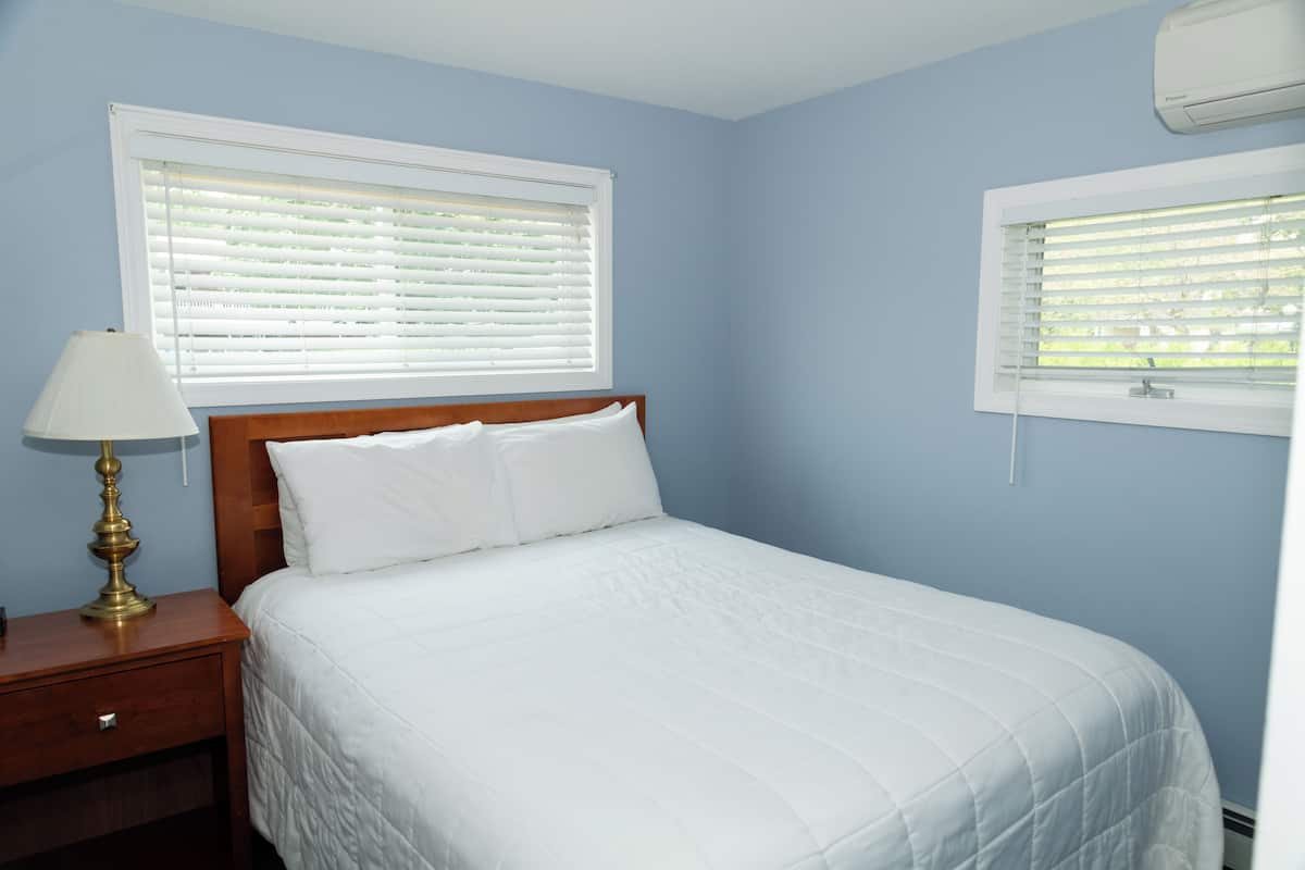 A bedroom with a bed, a nightstand, a lamp, and a window with blinds.