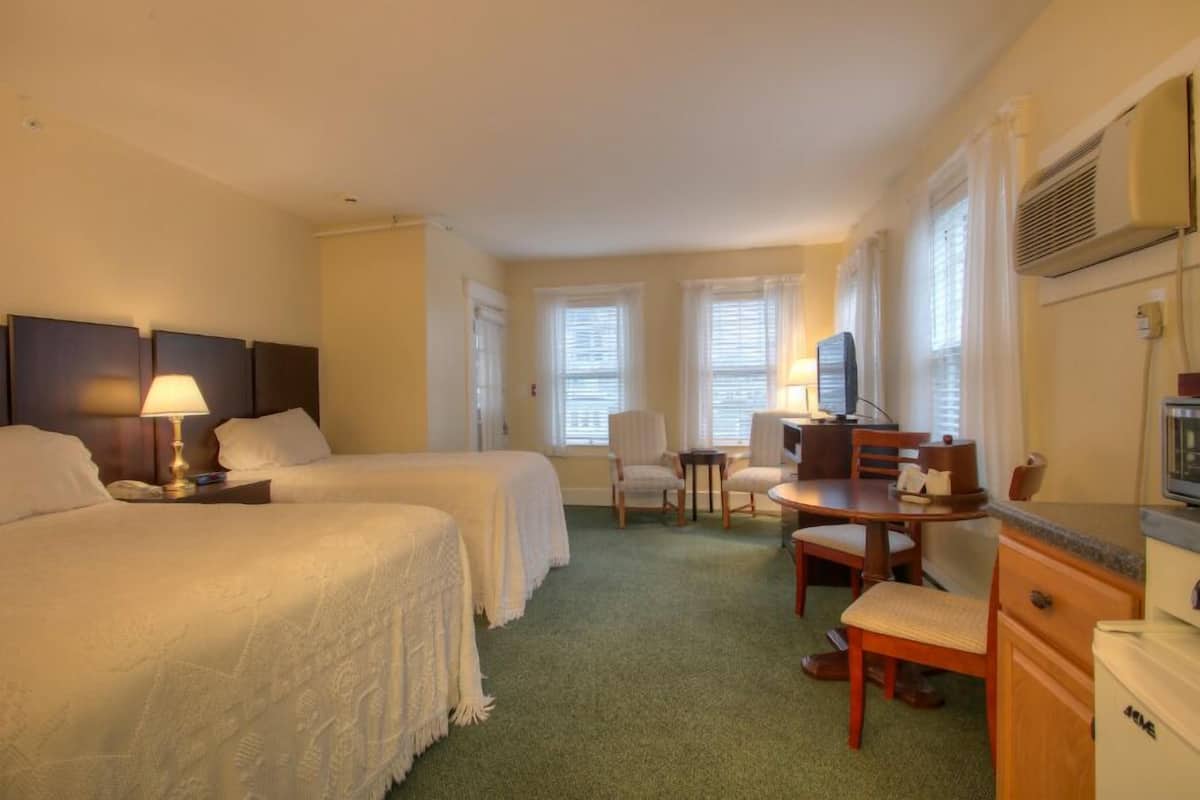 A hotel room with two beds, a desk, a chair, a TV, and a kitchenette.