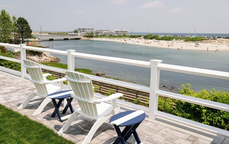 A waterfront patio with Adirondack chairs and a view of a beach and ocean.