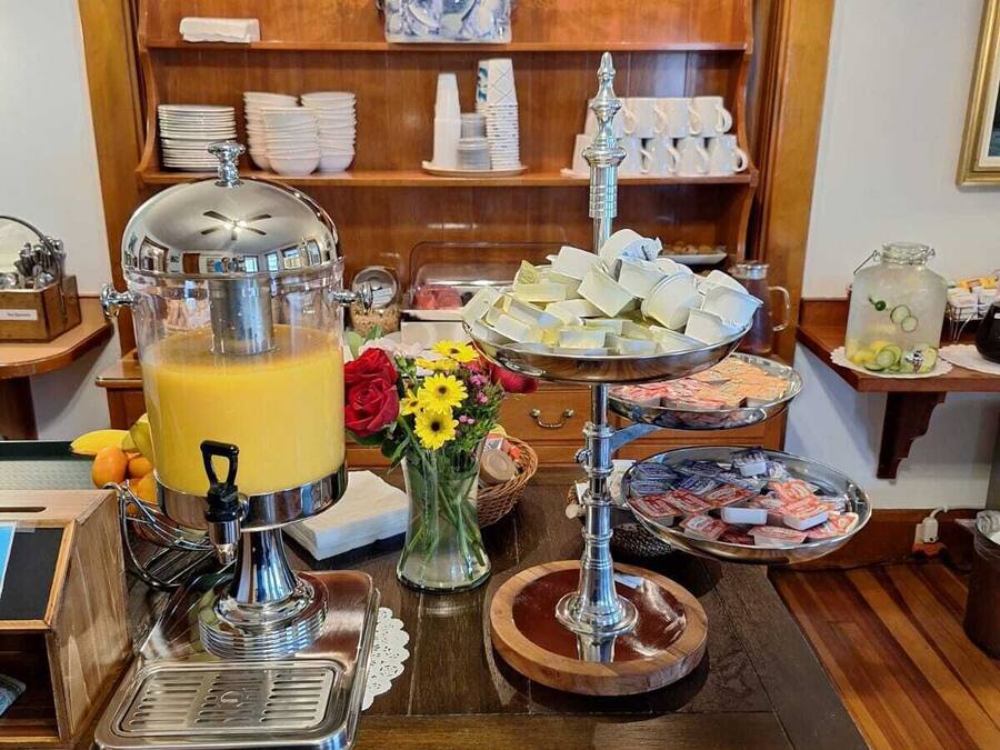 Montaje de bufé con dispensador de jugo, diferentes opciones de comida y un jarrón decorativo con flores.