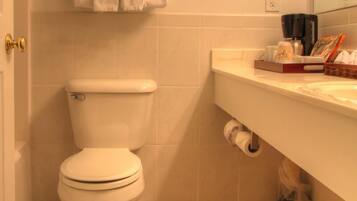 A bathroom with a toilet, a towel rack with towels, a coffee maker, and toiletries on the counter.