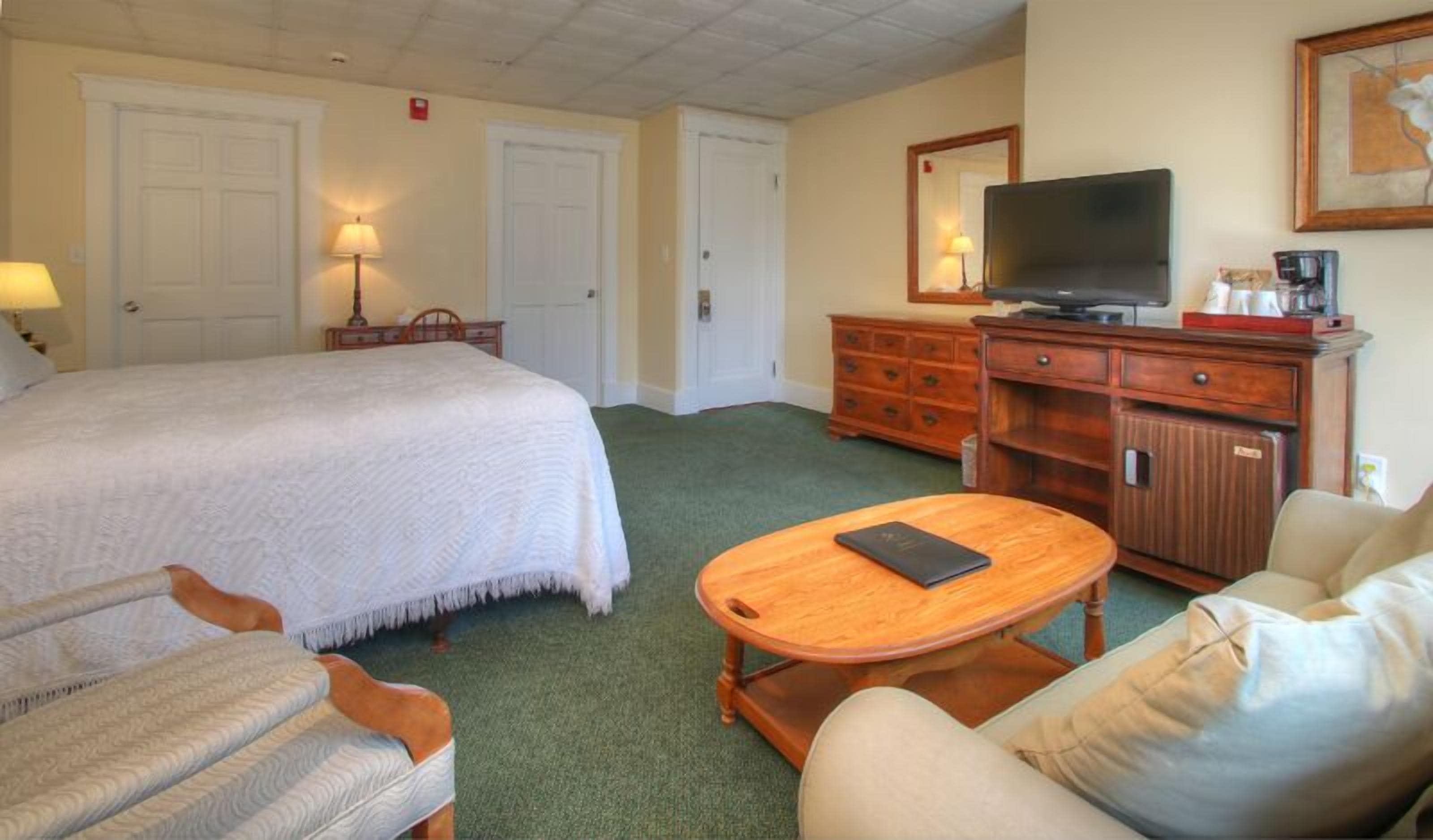 Une chambre d’hôtel avec un grand lit, une commode en bois, une télévision et une petite table ronde.