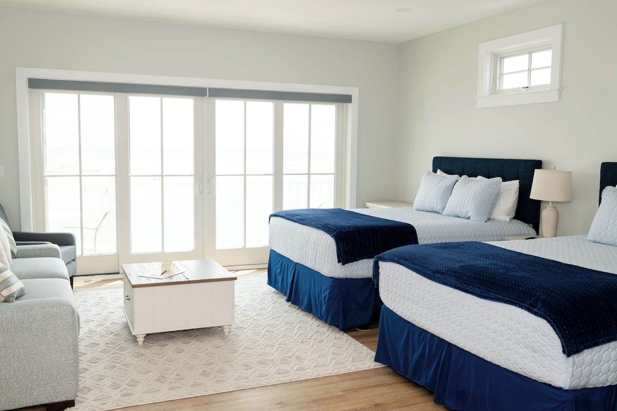A hotel room with two beds, a white dresser, a gray sofa, and a large window with a view.