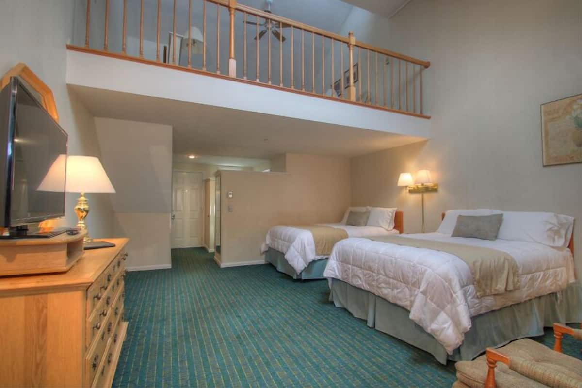 A hotel room with two beds, a TV, a dresser, and a balcony.