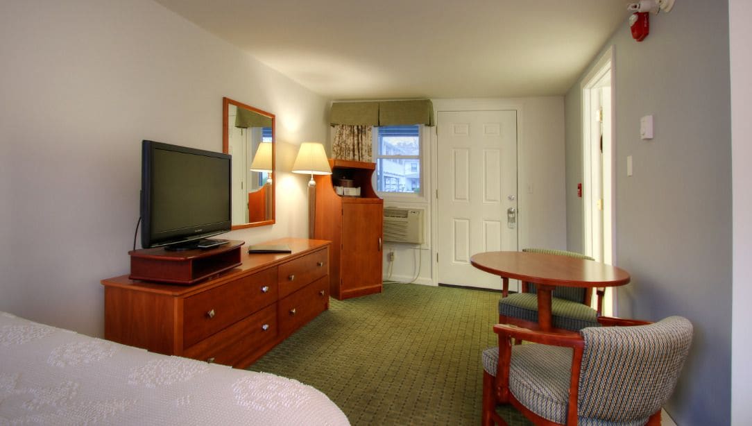 A hotel room with a bed, a TV, a dresser, a lamp, a small table, and a chair.