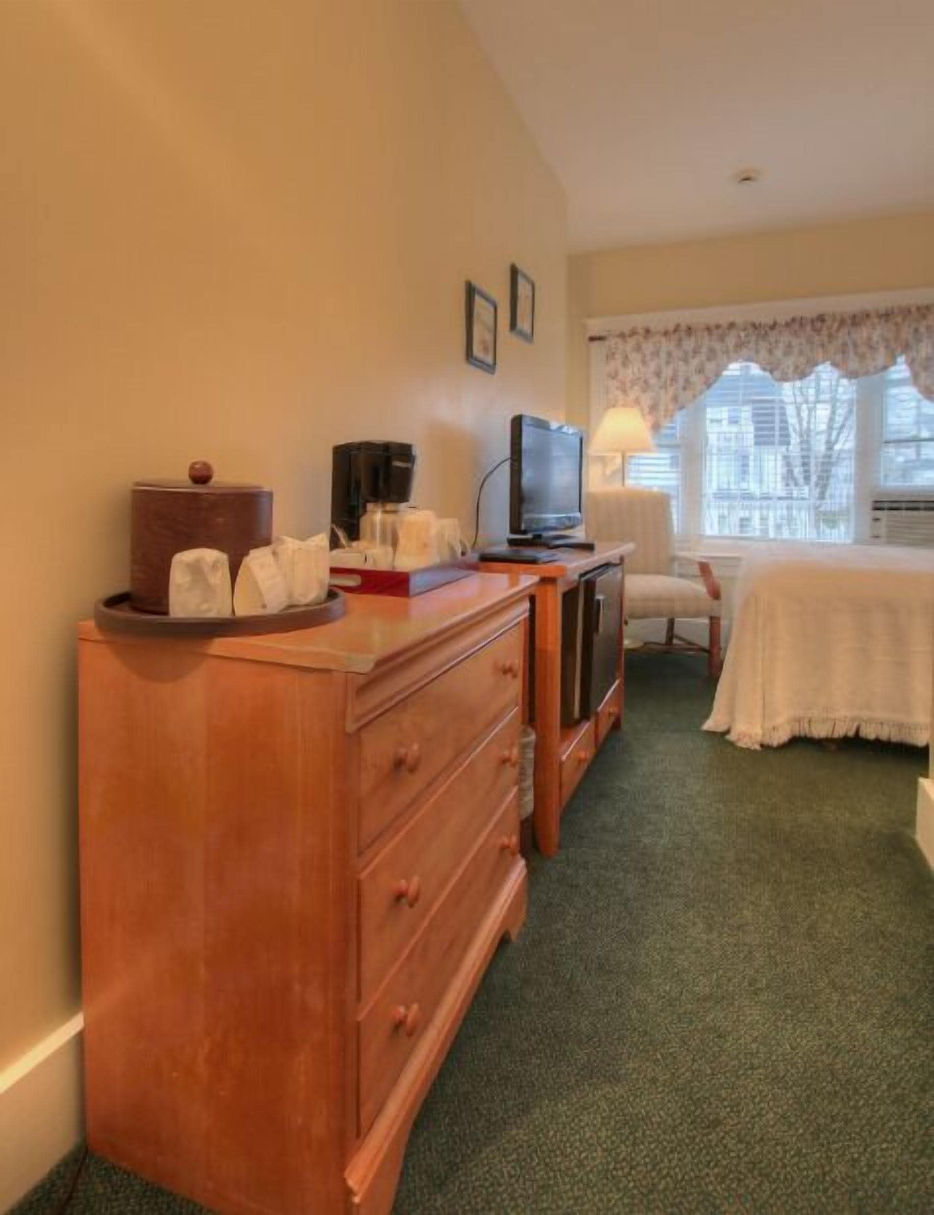 A hotel room with a wooden dresser, a television, a coffee maker, and a bed with a white bedspread.