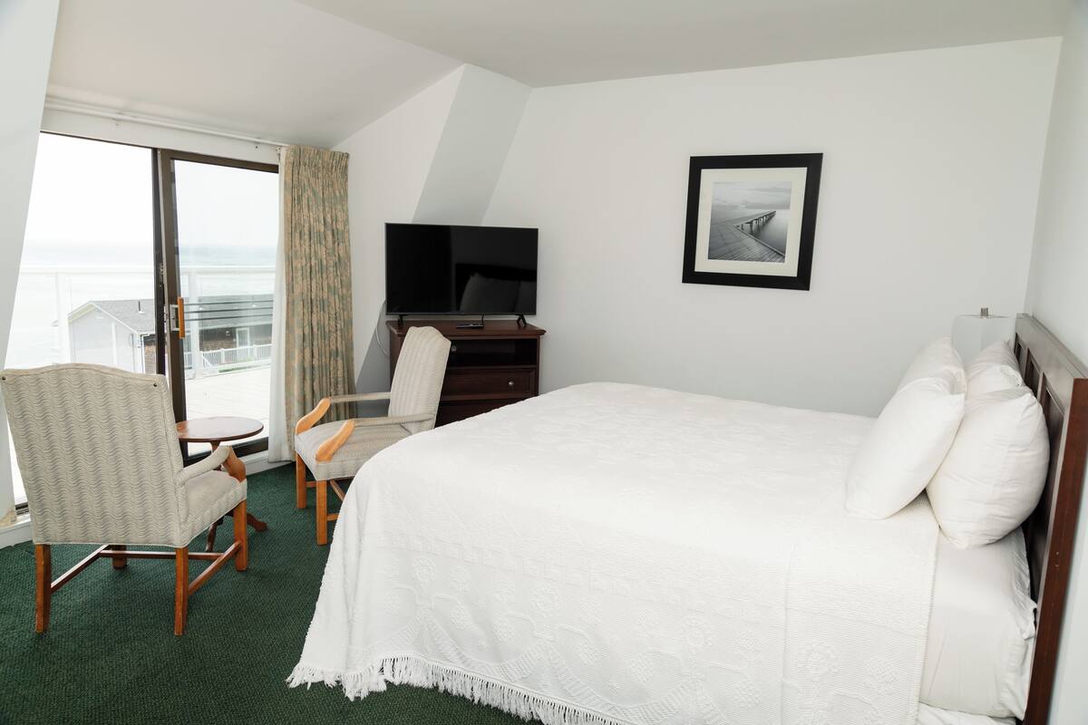 A hotel room with a bed, a television, a chair, and a view of the ocean.