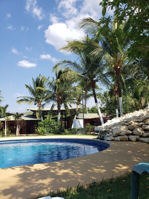 A pool area with palm trees, a stone wall, and a building with a tiled roof.