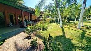 A building with a covered outdoor area, surrounded by a well-maintained garden with palm trees and various plants. - Angels Ecolodge (Veintisiete de Abril)