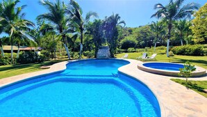 A large, clear swimming pool with a stone border, surrounded by palm trees and a well-maintained lawn. - Angels Ecolodge (Veintisiete de Abril)